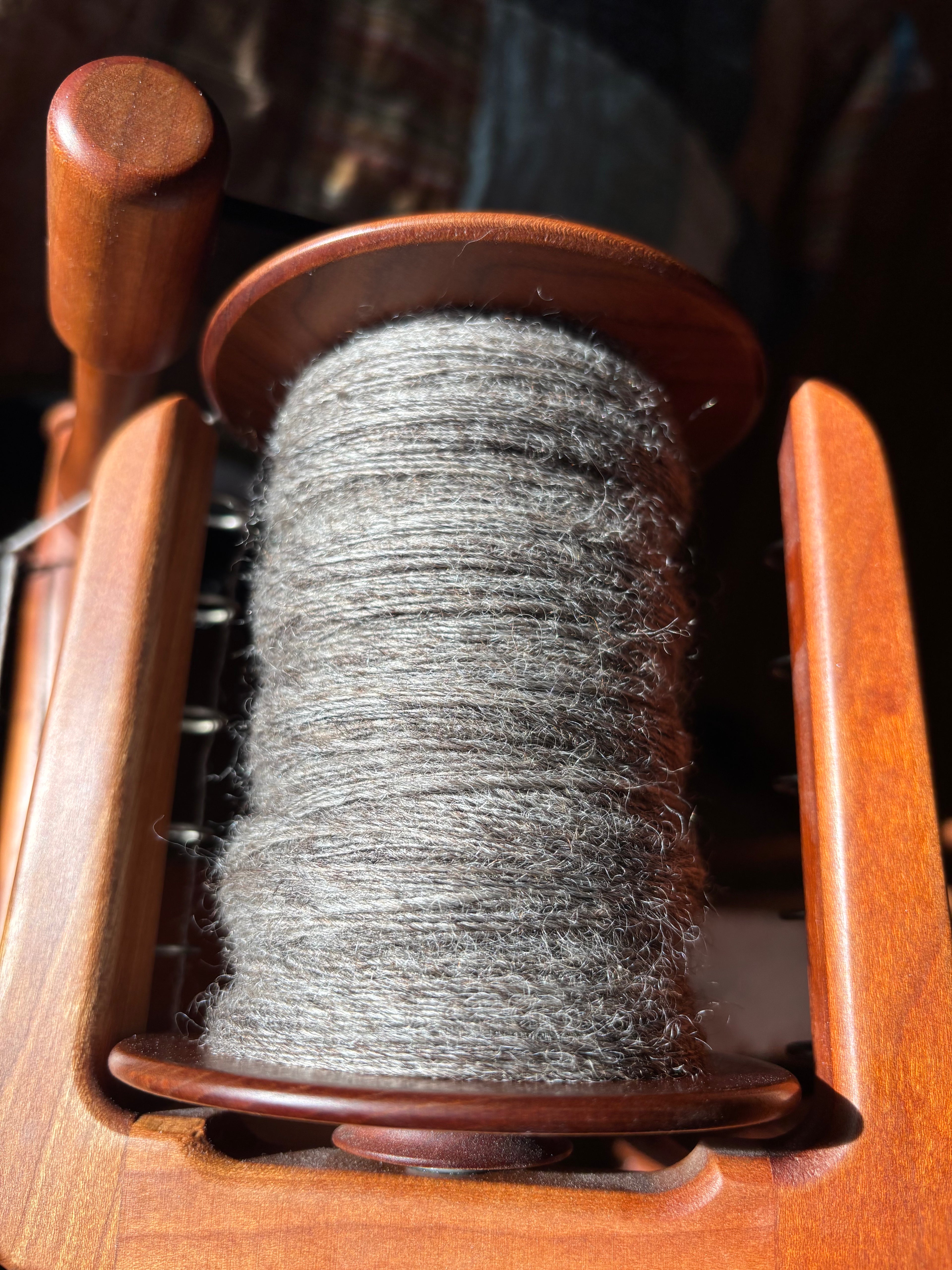 Spool of gray wool romney yarn on a wooden spinning wheel