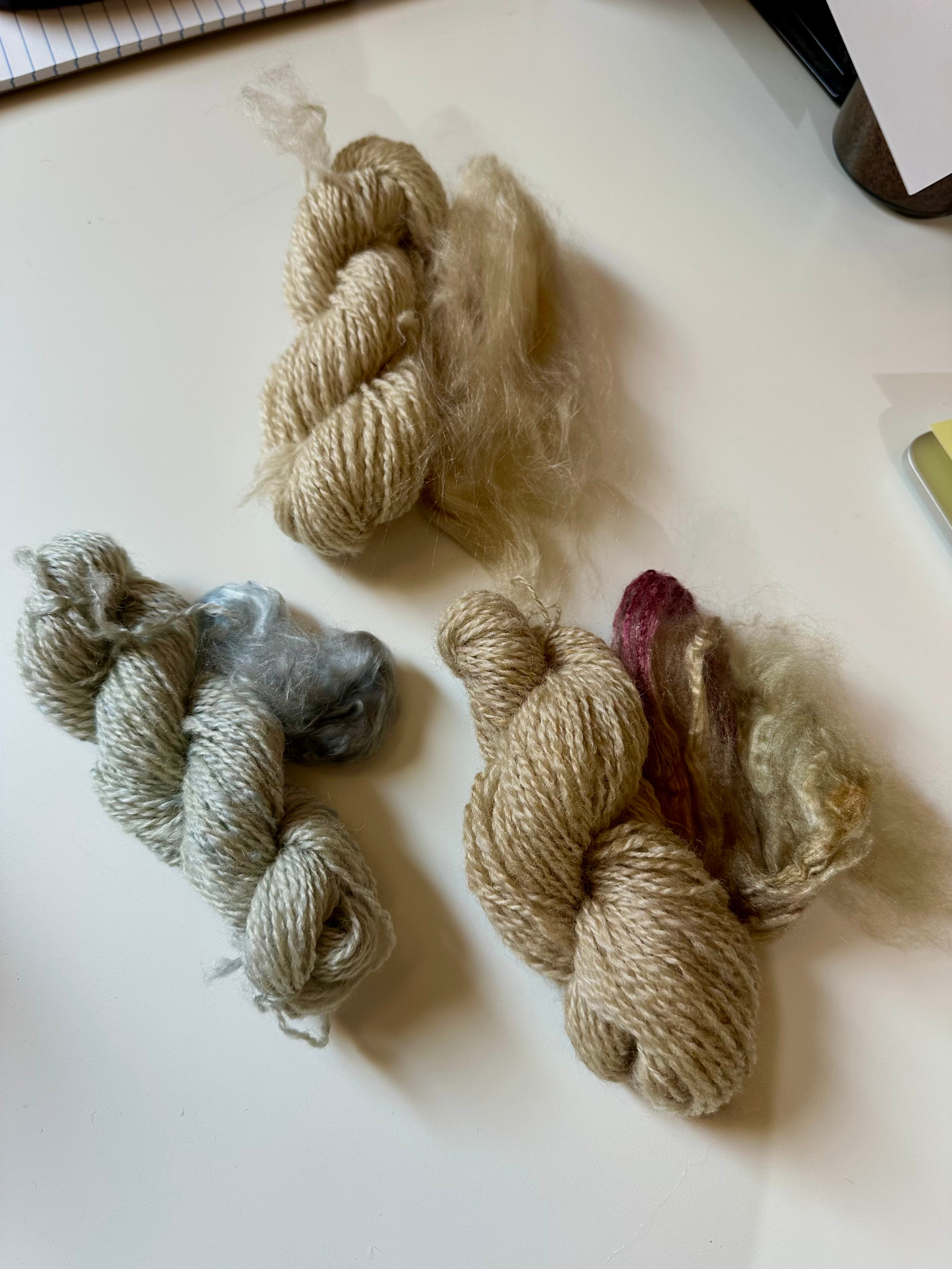 Three skeins of wool and silk yarn in different colors on a light surface.